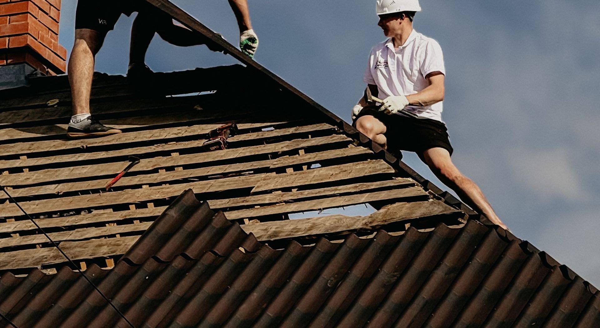 Deux couvreurs reprenant une toiture, liteaux mis à nu sous un ciel couvert